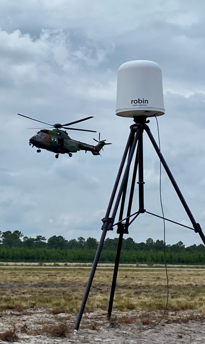 Military helicopter flying over a line of trees in a cloudy sky, monitored by an IRIS drone detection radar